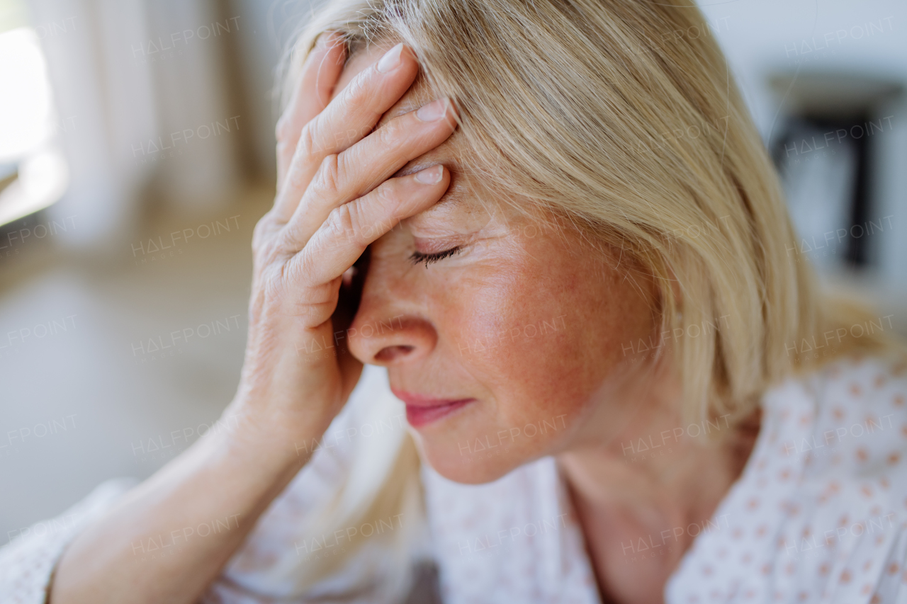 A portrait of an attractive senior woman sitting on a sofa at home with a headache