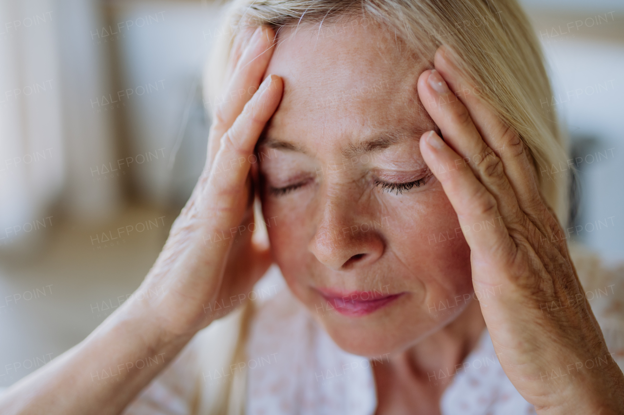 A portrait of an attractive senior woman sitting on a sofa at home with a headache