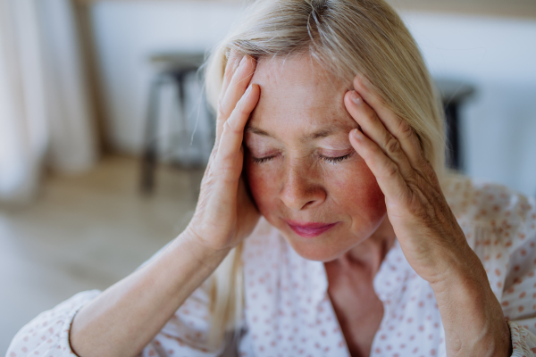 A portrait of an attractive senior woman sitting on a sofa at home with a headache