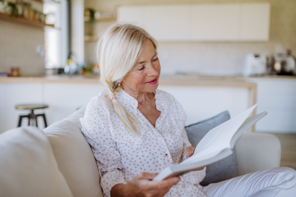 A senior woman sitting on sofa and reading book at home