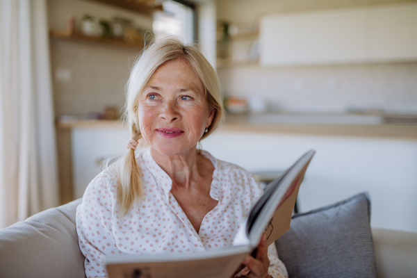 A senior woman sitting on sofa and reading book at home