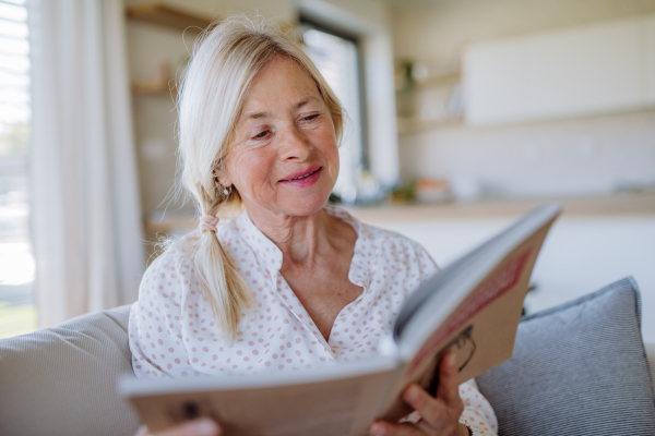 A senior woman sitting on sofa and reading book at home