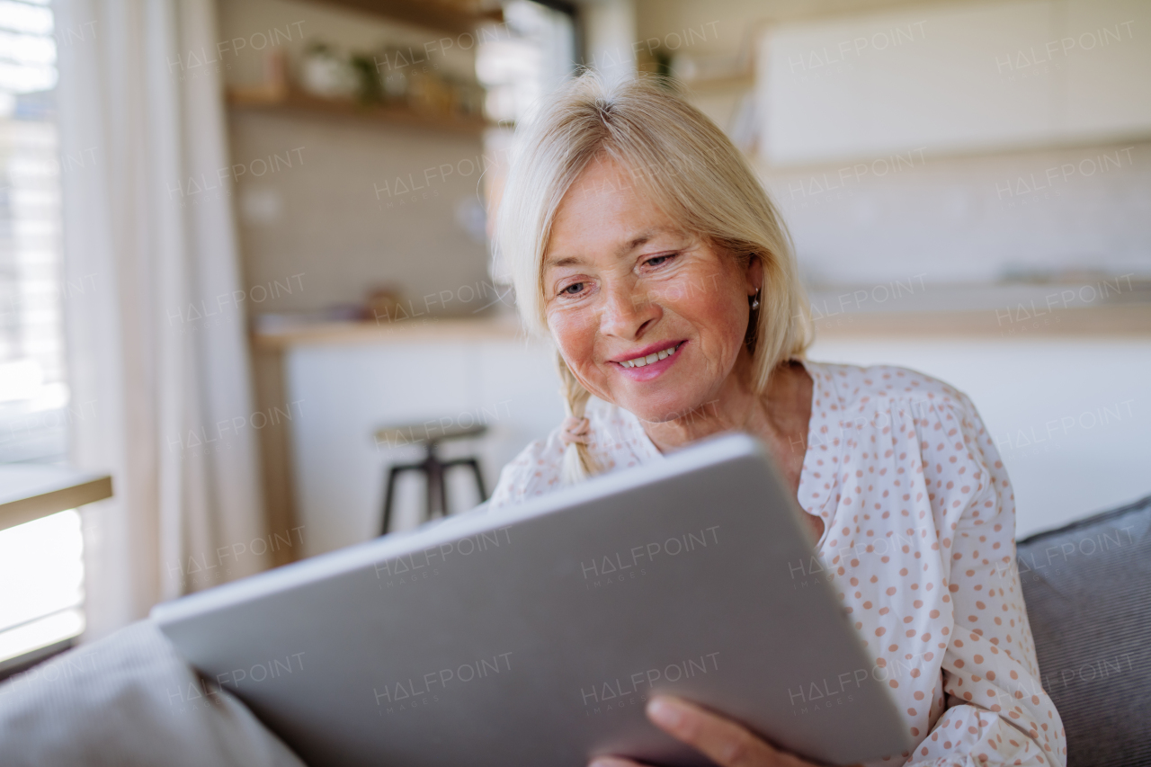 A senior woman sitting on sofa and rusing tablet at home