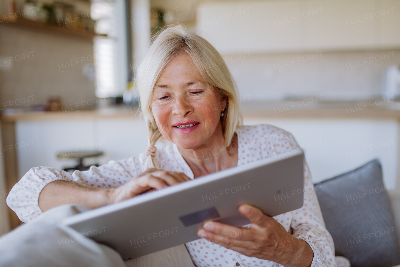 A senior woman sitting on sofa and rusing tablet at home