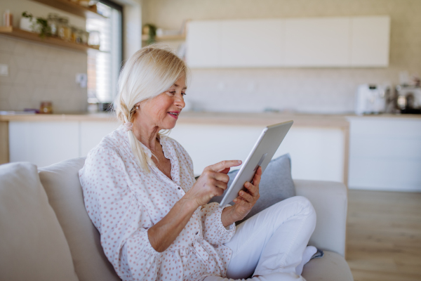 A senior woman sitting on sofa and rusing tablet at home