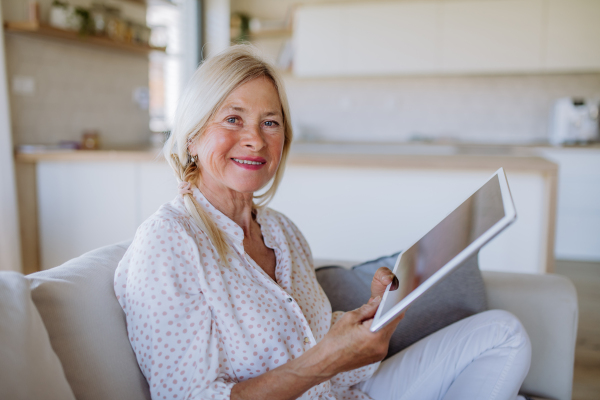 A senior woman sitting on sofa and rusing tablet at home