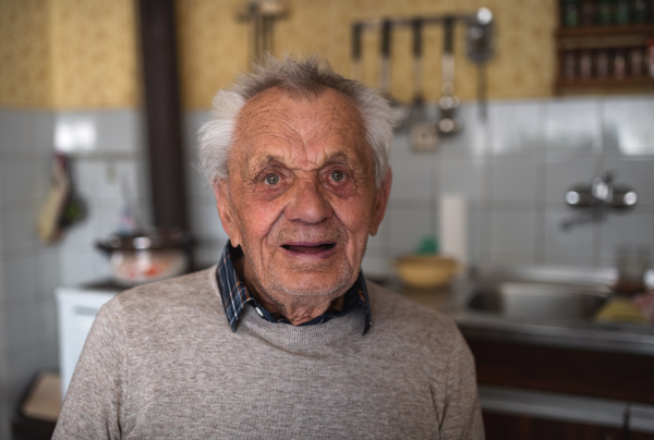 A portrait of elderly man standing indoors at home, laughing.