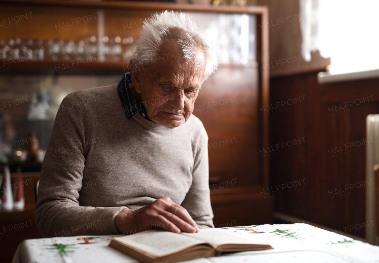 A portrait of elderly man sitting at the table indoors at home, resting.