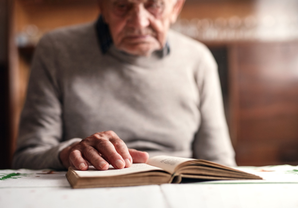 A portrait of elderly man sitting at the table indoors at home, resting and reading bible.