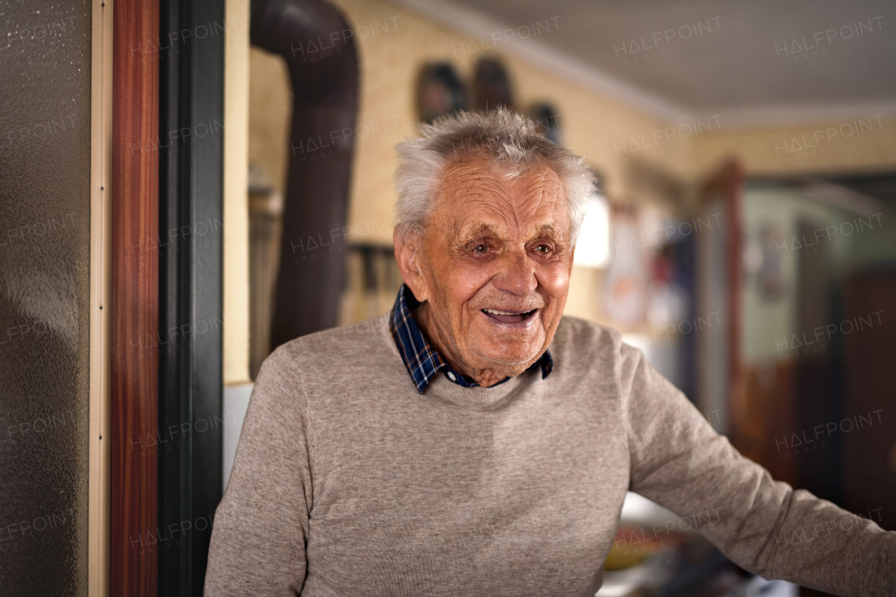 A portrait of elderly man standing indoors at home, laughing.