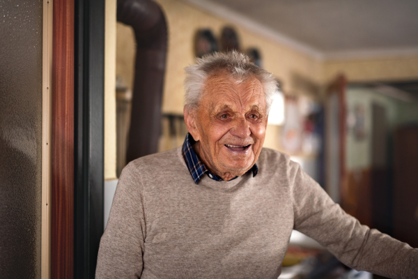 A portrait of elderly man standing indoors at home, laughing.