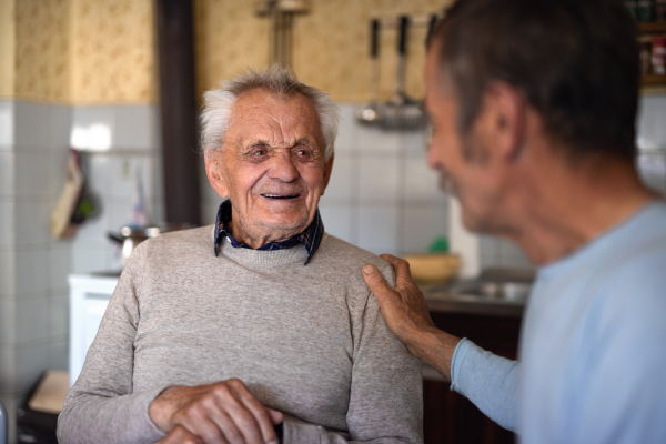 A portrait of man with elderly father sitting at the table indoors at home, talking.