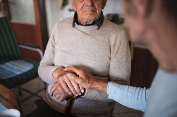 Midsection of unrecognizable man with elderly father sitting at the table indoors at home, talking.