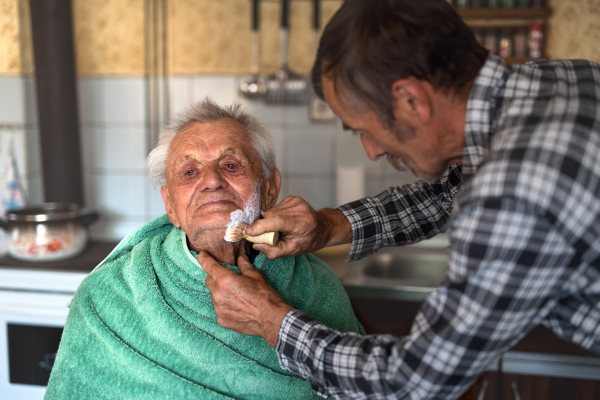 Portrait of man shaving happy elderly father indoors at home.