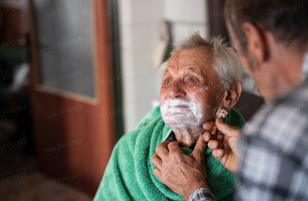 Portrait of man shaving happy elderly father indoors at home.