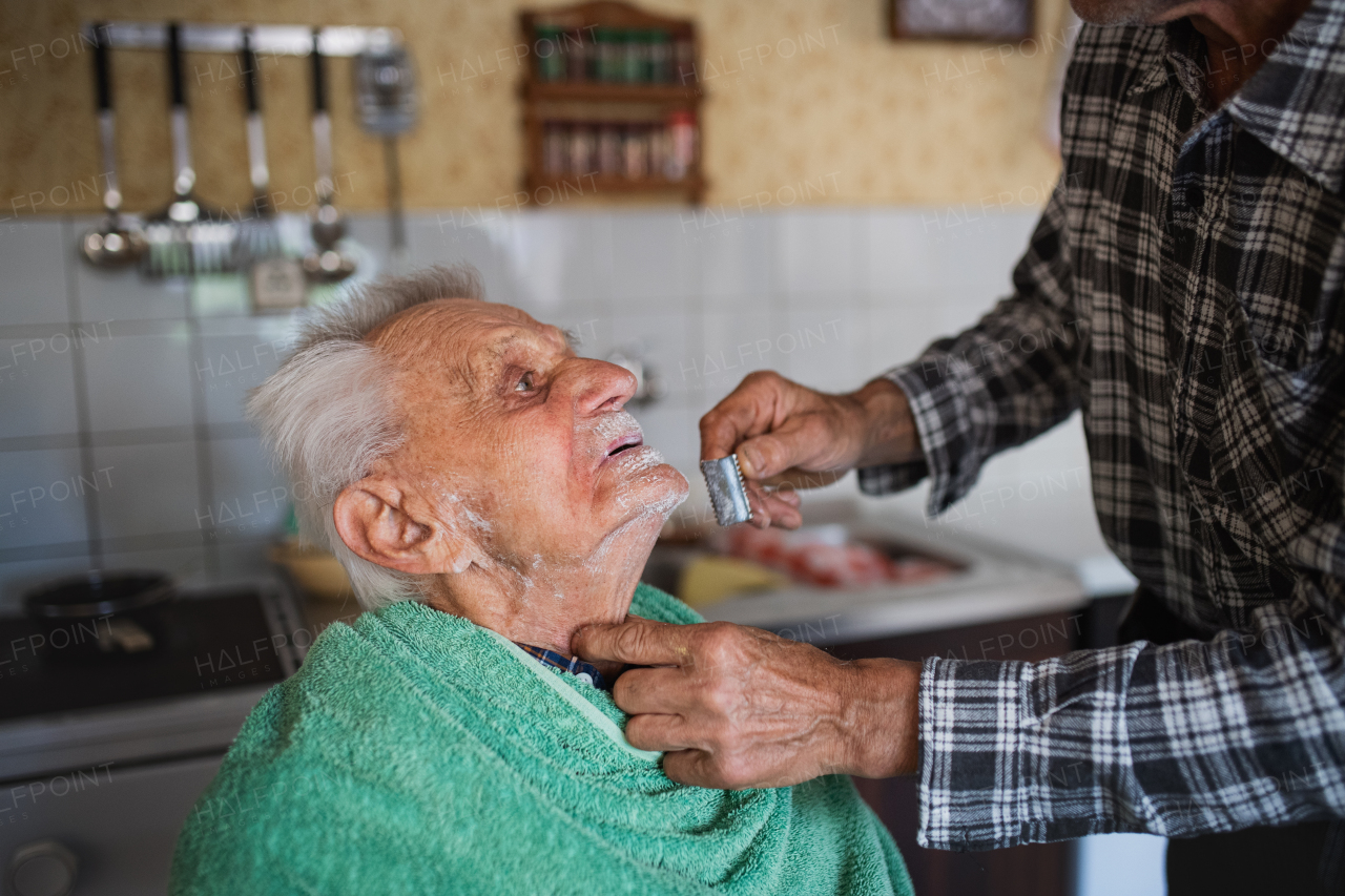 Portrait of man shaving happy elderly father indoors at home.