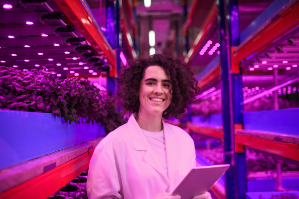 Portrait of worker with tablet looking at camera on aquaponic farm, sustainable business and artificial lighting.