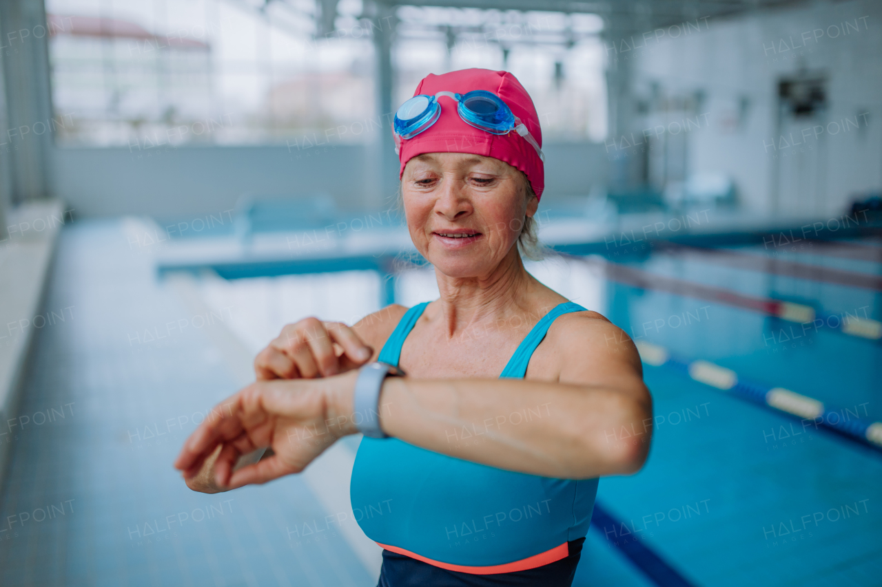 A senior woman setting smartwatch before swim in indoors swimming pool.