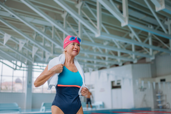 A low angle view of active senior woman preapring for swim in indoors swimming pool.