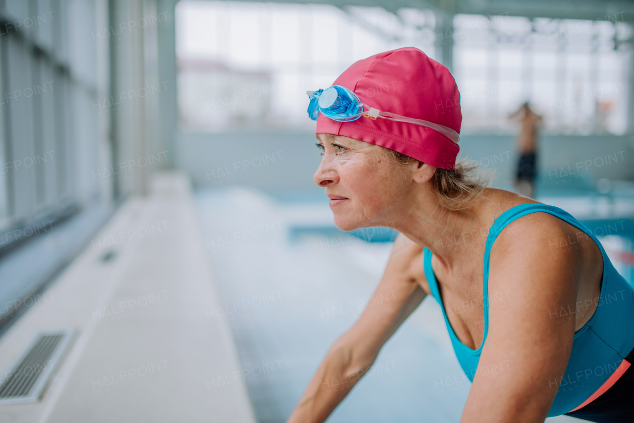 An active senior woman preapring for swim in indoors swimming pool.