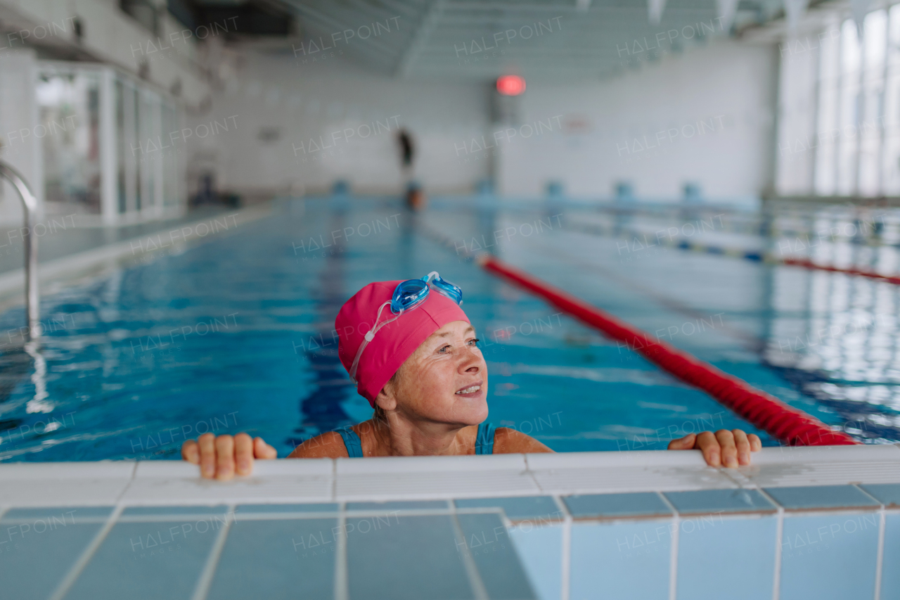 A happy senior woman in swimming pool, holding on edge.