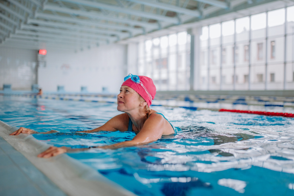 A happy senior woman in swimming pool, holding on edge.