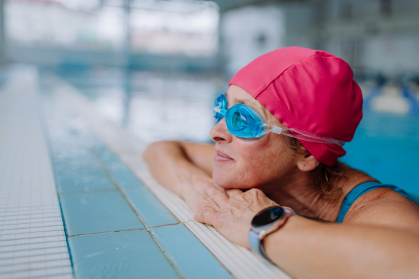 A happy senior woman in swimming pool, leaning on edge.