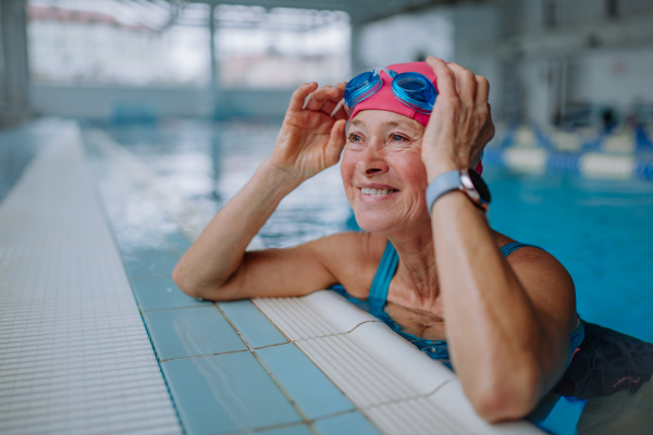 A happy senior woman in swimming pool, leaning on edge.