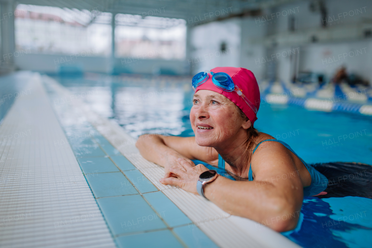 A happy senior woman in swimming pool, leaning on edge.