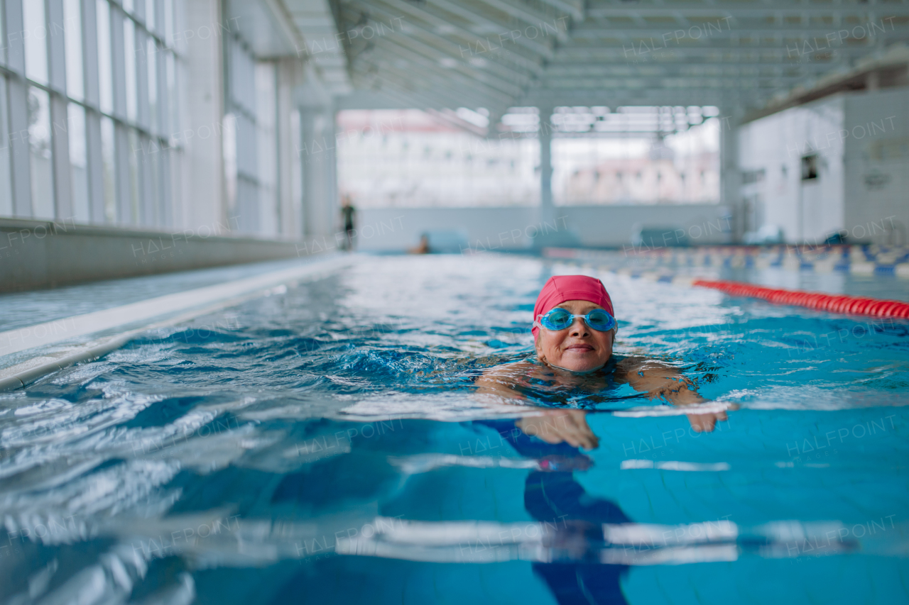 An active senior woman swimming in indoors swimming pool.