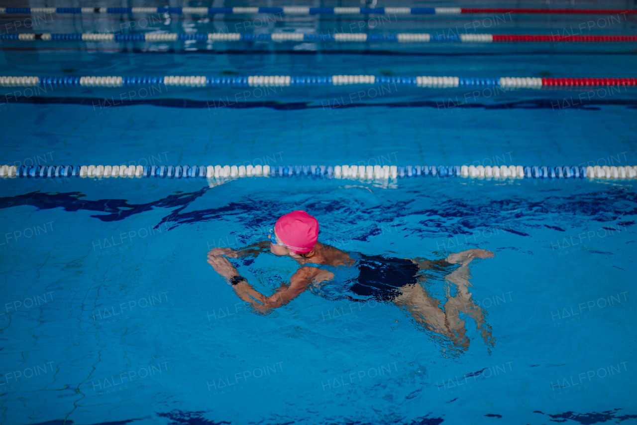 A high angle view of active senior woman swimming in indoors swimming pool.