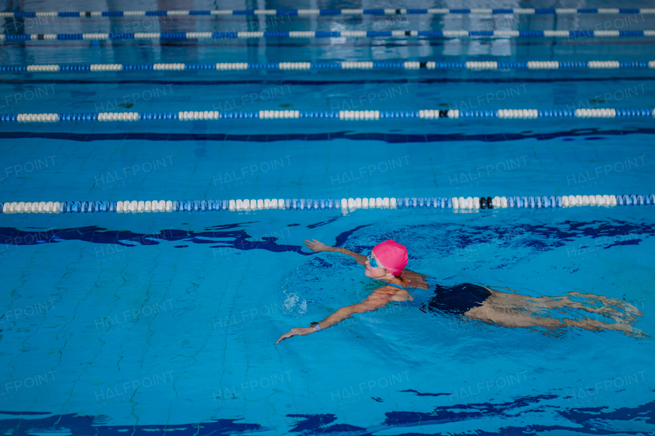 A high angle view of active senior woman swimming in indoors swimming pool.