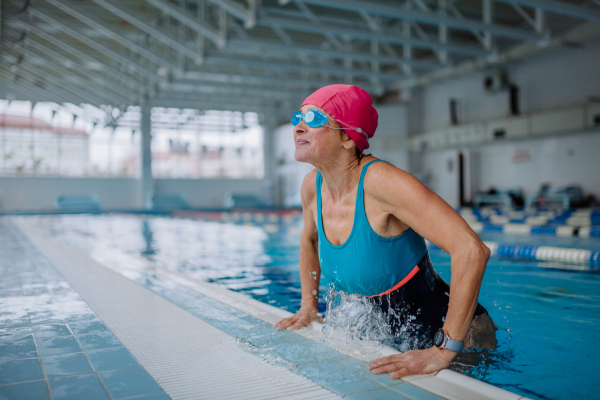 A happy senior woman getting out of the swimming pool indoors.