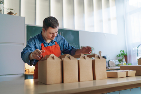 A cheerful young Down Syndrome waiter working in take away restaurant, social inclusion concept.