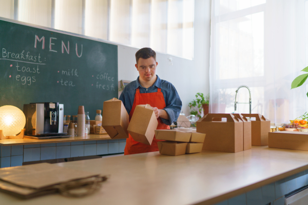 A cheerful young Down Syndrome waiter working in take away restaurant, social inclusion concept.