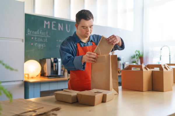 A cheerful young Down Syndrome waiter working in take away restaurant, social inclusion concept.