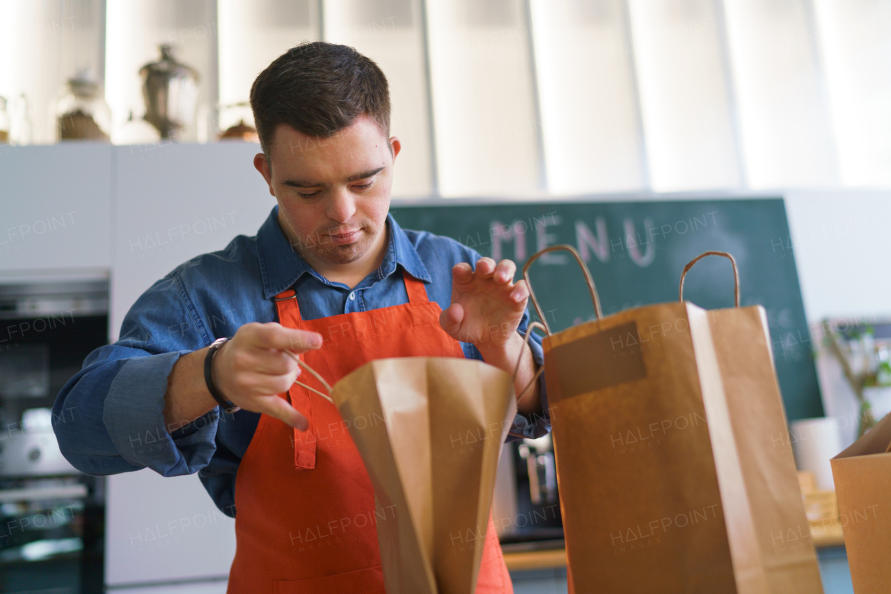 A cheerful young Down Syndrome waiter working in take away restaurant, social inclusion concept.