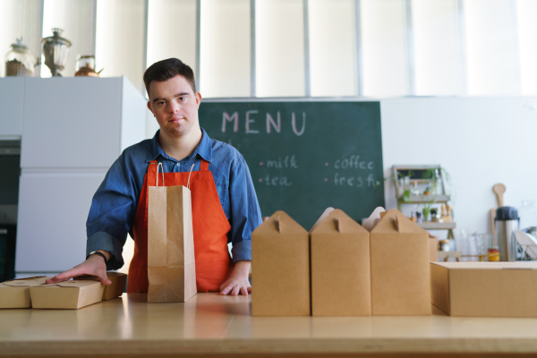 A cheerful young Down Syndrome waiter working in take away restaurant, social inclusion concept.