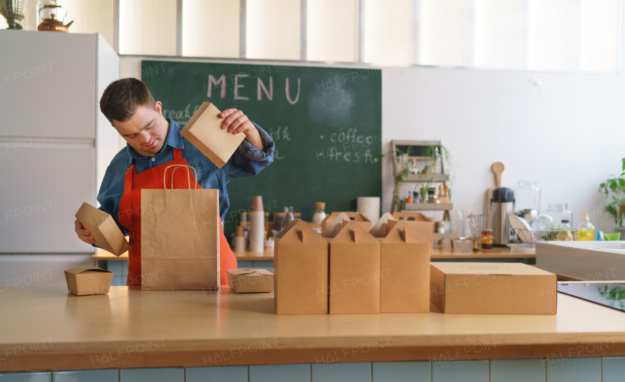 A cheerful young Down Syndrome waiter working in take away restaurant, social inclusion concept.