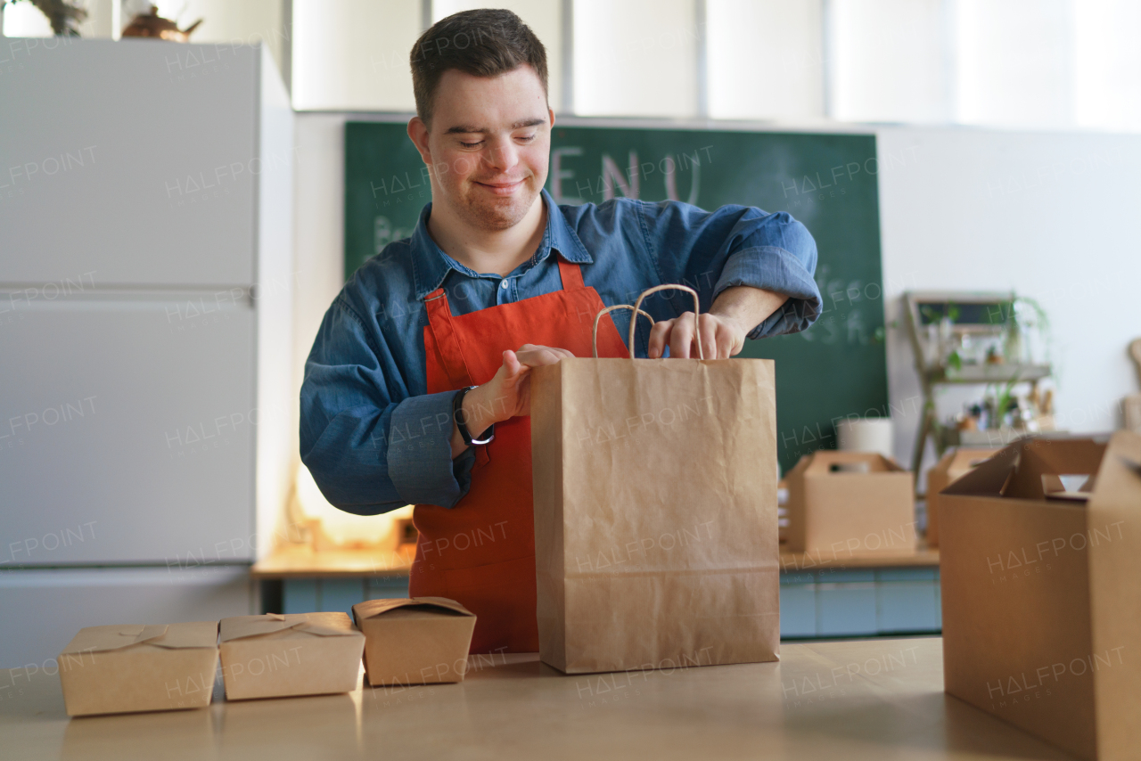 A cheerful young Down Syndrome waiter working in take away restaurant, social inclusion concept.