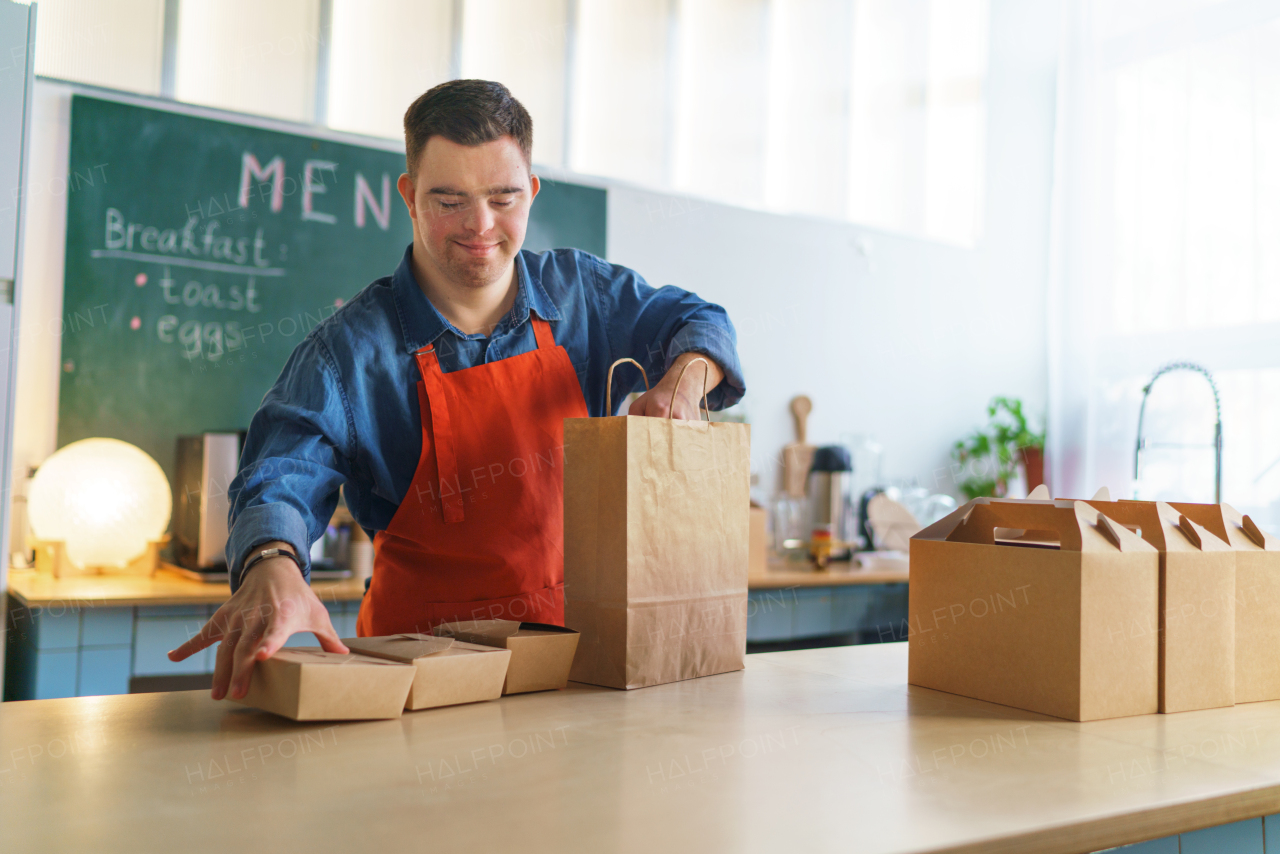 A cheerful young Down Syndrome waiter working in take away restaurant, social inclusion concept.