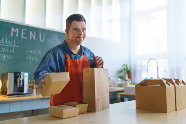 A cheerful young Down Syndrome waiter working in take away restaurant, social inclusion concept.