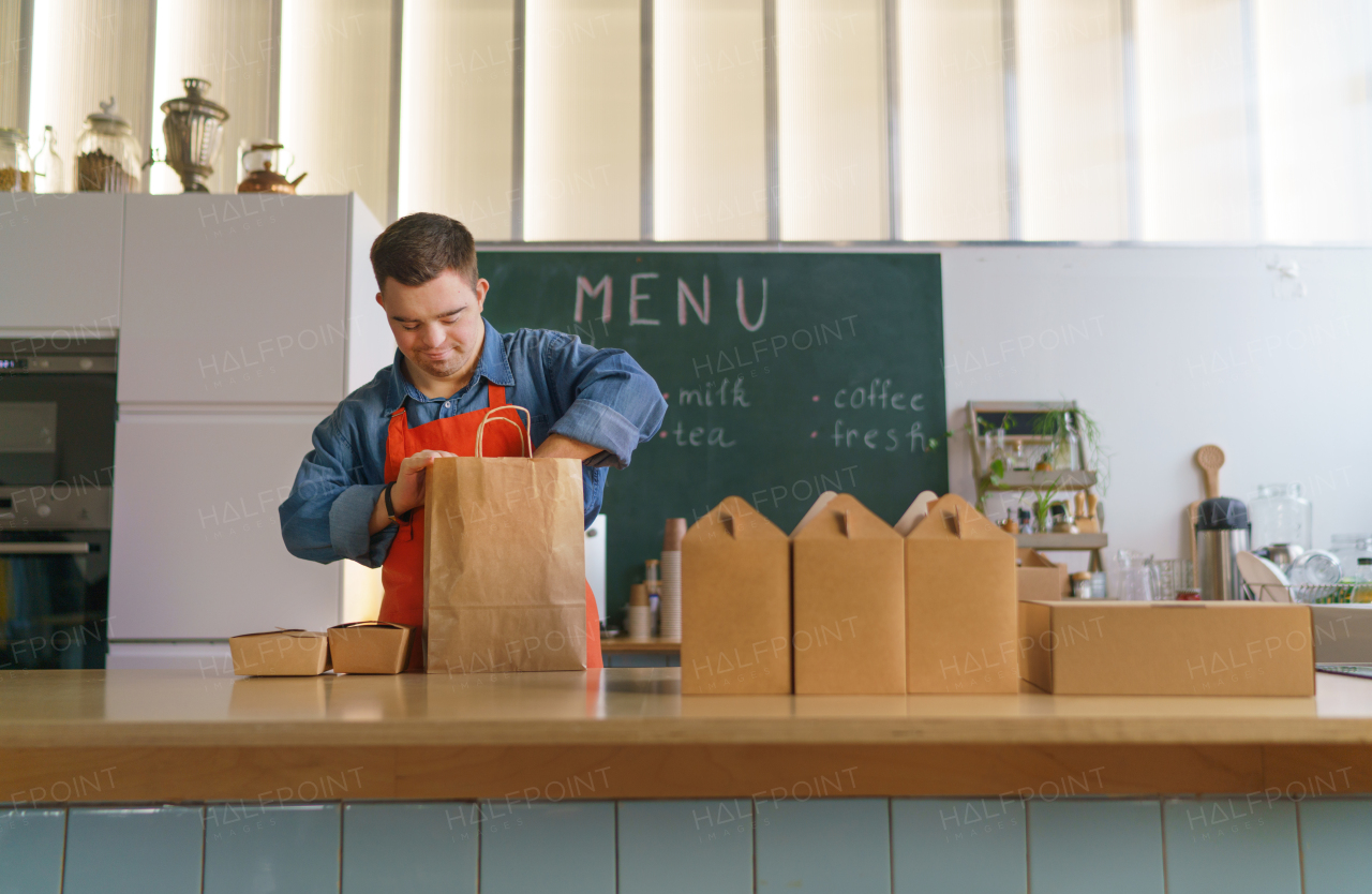 A cheerful young Down Syndrome waiter working in take away restaurant, social inclusion concept.