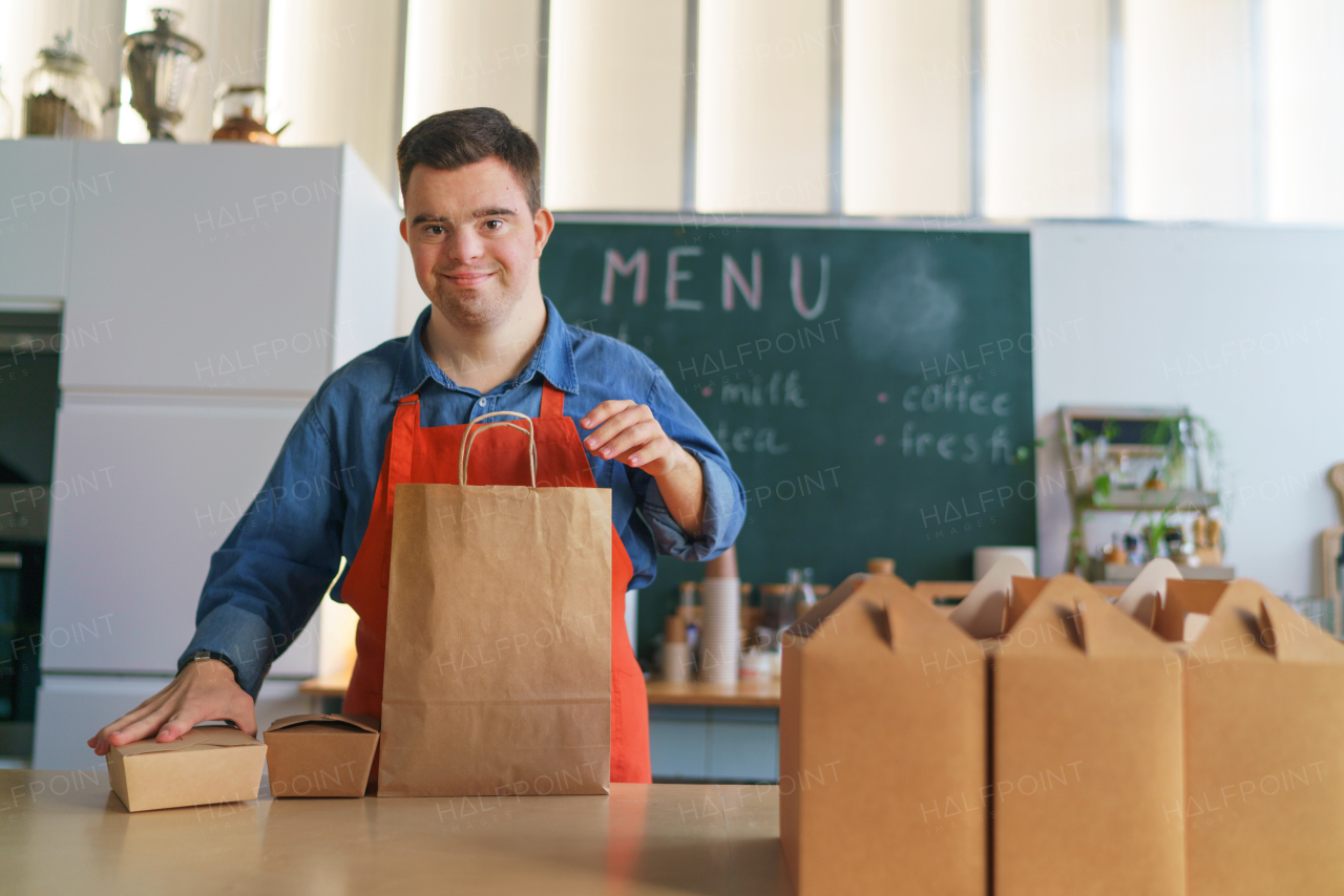 A cheerful young Down Syndrome waiter working in take away restaurant, social inclusion concept.