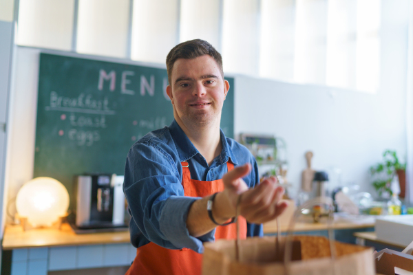 A cheerful young Down Syndrome waiter working in take away restaurant, social inclusion concept.