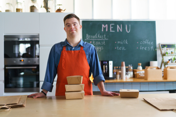 A cheerful young Down Syndrome waiter working in take away restaurant, social inclusion concept.