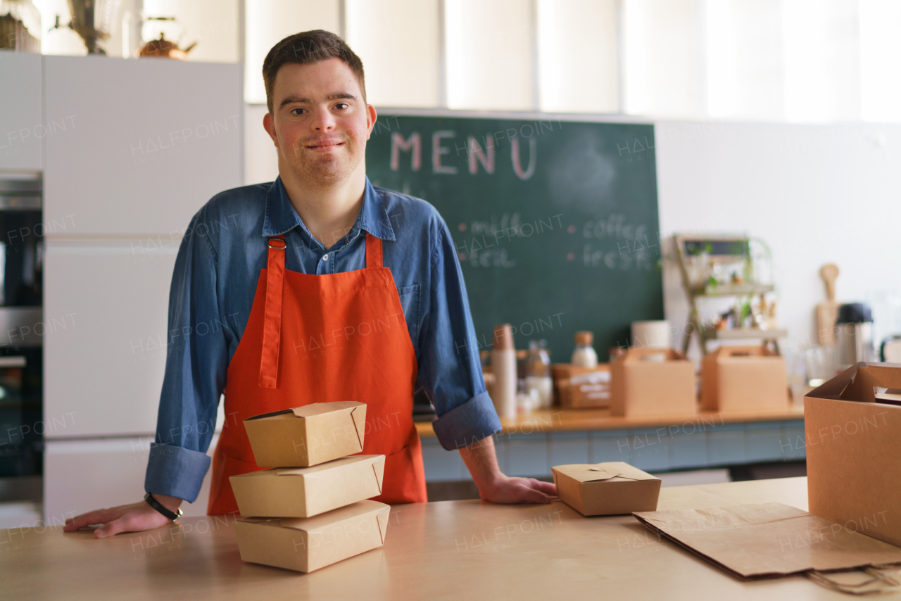 A cheerful young Down Syndrome waiter working in take away restaurant, social inclusion concept.