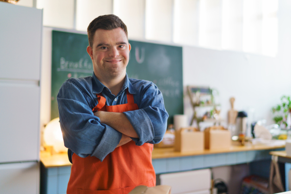 A cheerful young Down Syndrome waiter working in take away restaurant, social inclusion concept.