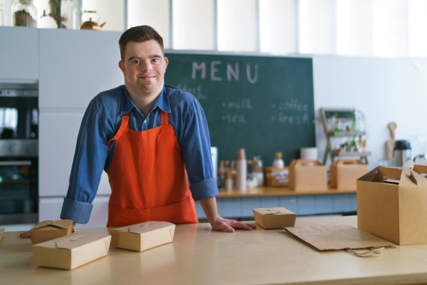 A cheerful young Down Syndrome waiter working in take away restaurant, social inclusion concept.