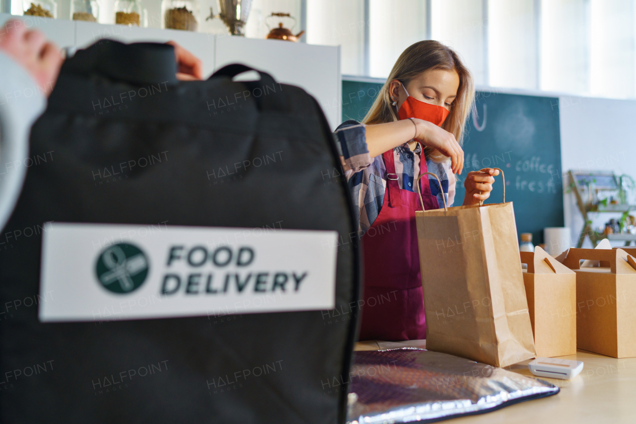 A young waiter packing take away meals for delivery in restaurant, coronavirus concept.